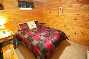 Une pièce aux murs lambrissés, avec un lit, un bureau et une lampe.