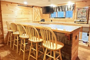 Un intérieur en bois avec un coin bar, des chaises en bois, un téléviseur et une fenêtre avec des rideaux.