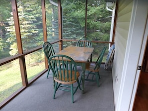 Une terrasse couverte avec une table et des chaises, de grandes fenêtres et une vue sur les arbres.