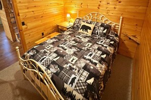 A wooden cabin-style bedroom with a metal bed frame, a plaid-patterned bedspread, and a nightstand with a lamp.