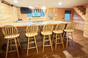 Un espace bar en bois, doté d’un long comptoir et de quatre chaises en bois.