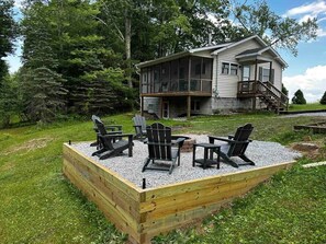 Une maison dotée d’une terrasse, entourée d’une zone également aménagée en terrasse avec des chaises Adirondack en bois.