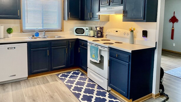 A modern kitchen with dark cabinets, a white countertop, a microwave, a stove, and a sink. - Remodeled apartment in central location (Council Bluffs)