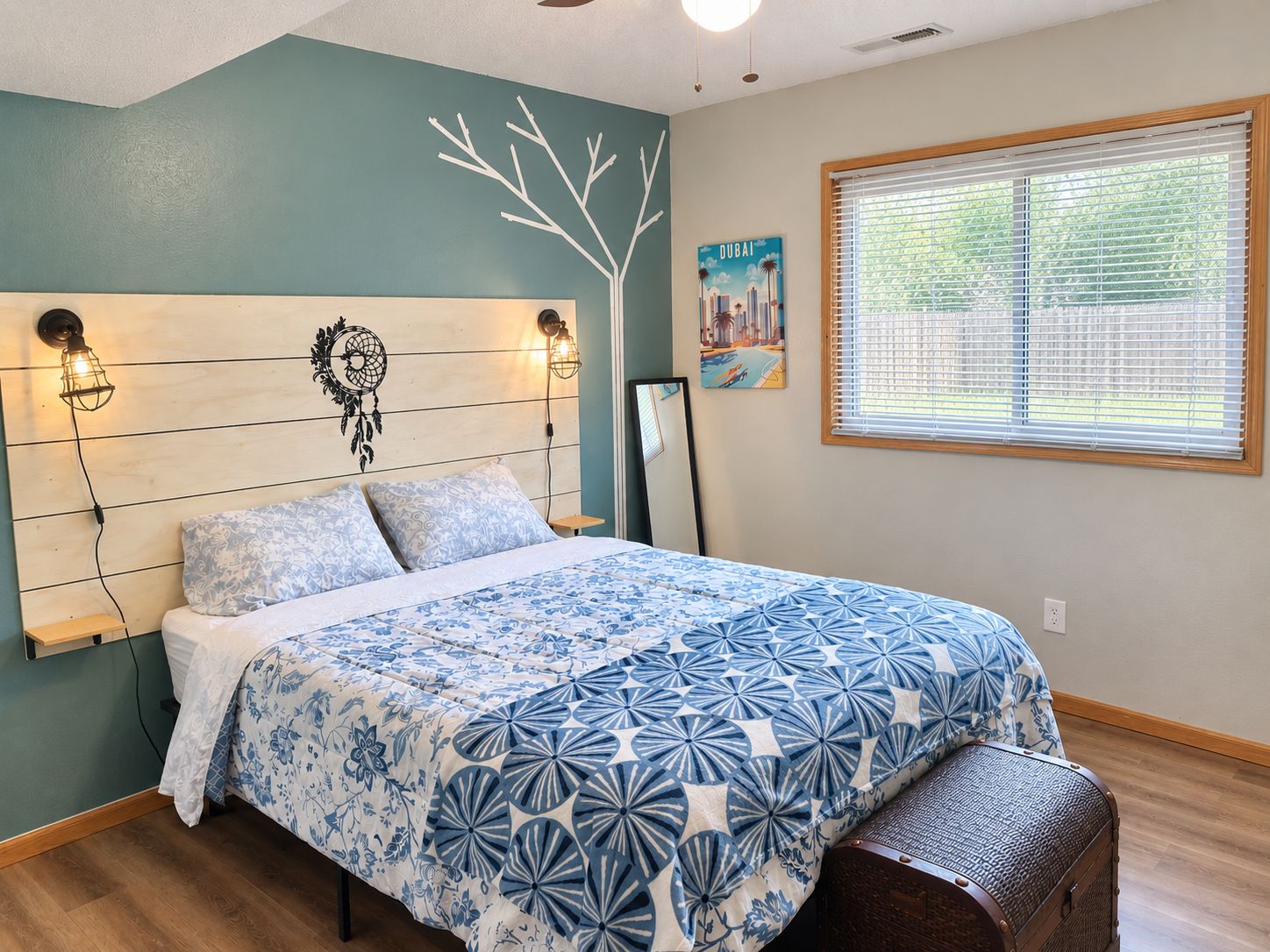 A bedroom with a bed, a headboard with wall-mounted lights, a window with blinds, and a wall painting.