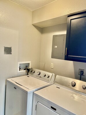 A laundry room with two white front-loading washers and dryers, a small electrical panel, and a blue cabinet above the dryers. - Remodeled apartment in central location (Council Bluffs)