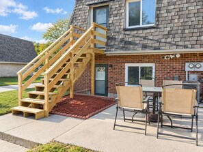 A residential house with a wooden staircase leading to a front door, a brick exterior, and a patio area with outdoor furniture. - Remodeled apartment in central location (Council Bluffs)