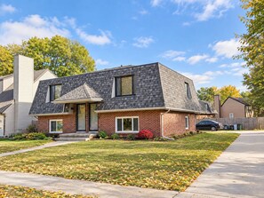 A two-story house with a brick facade, a grey shingled roof, and a front yard with grass and fallen leaves. - Remodeled apartment in central location (Council Bluffs)