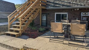 A two-story house with a wooden staircase leading to the second floor. There is a patio with outdoor furniture and a brick wall. - Remodeled apartment in central location (Council Bluffs)