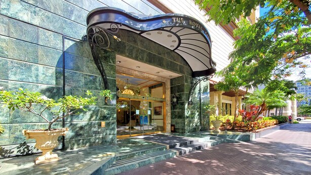 L’entrée d’un hôtel, avec un auvent incurvé, une enseigne indiquant « The Royal Garden at Waikiki », et un escalier menant à l’entrée.