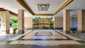 Un hall d’entrée spacieux avec une fontaine centrale, un sol carrelé et des plantes en pot.