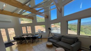 Amplia sala de estar con un sofá grande de color gris, piso de madera y amplias ventanas que ofrecen vistas al exterior.