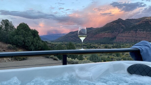 Tinaja con una copa de vino blanco, con vistas a un paisaje montañoso con árboles y un atardecer.