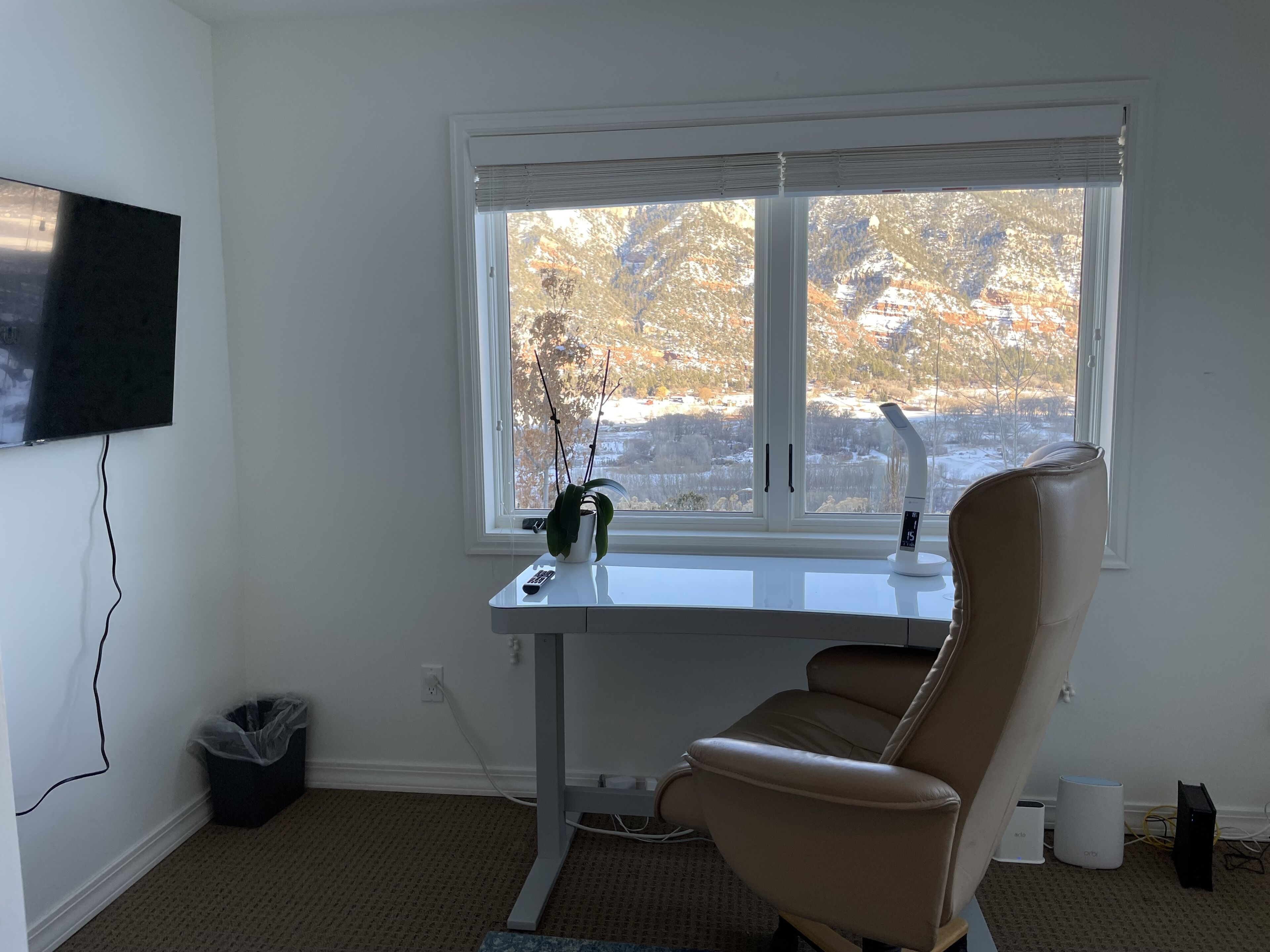 Una habitación con escritorio, silla, televisor y ventana con vistas a árboles y un paisaje nevado.