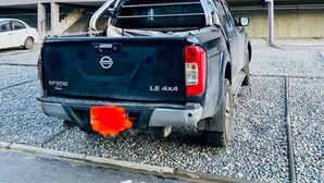 A Nissan NP300 Dinas truck parked in a gravel parking area with a building in the background.