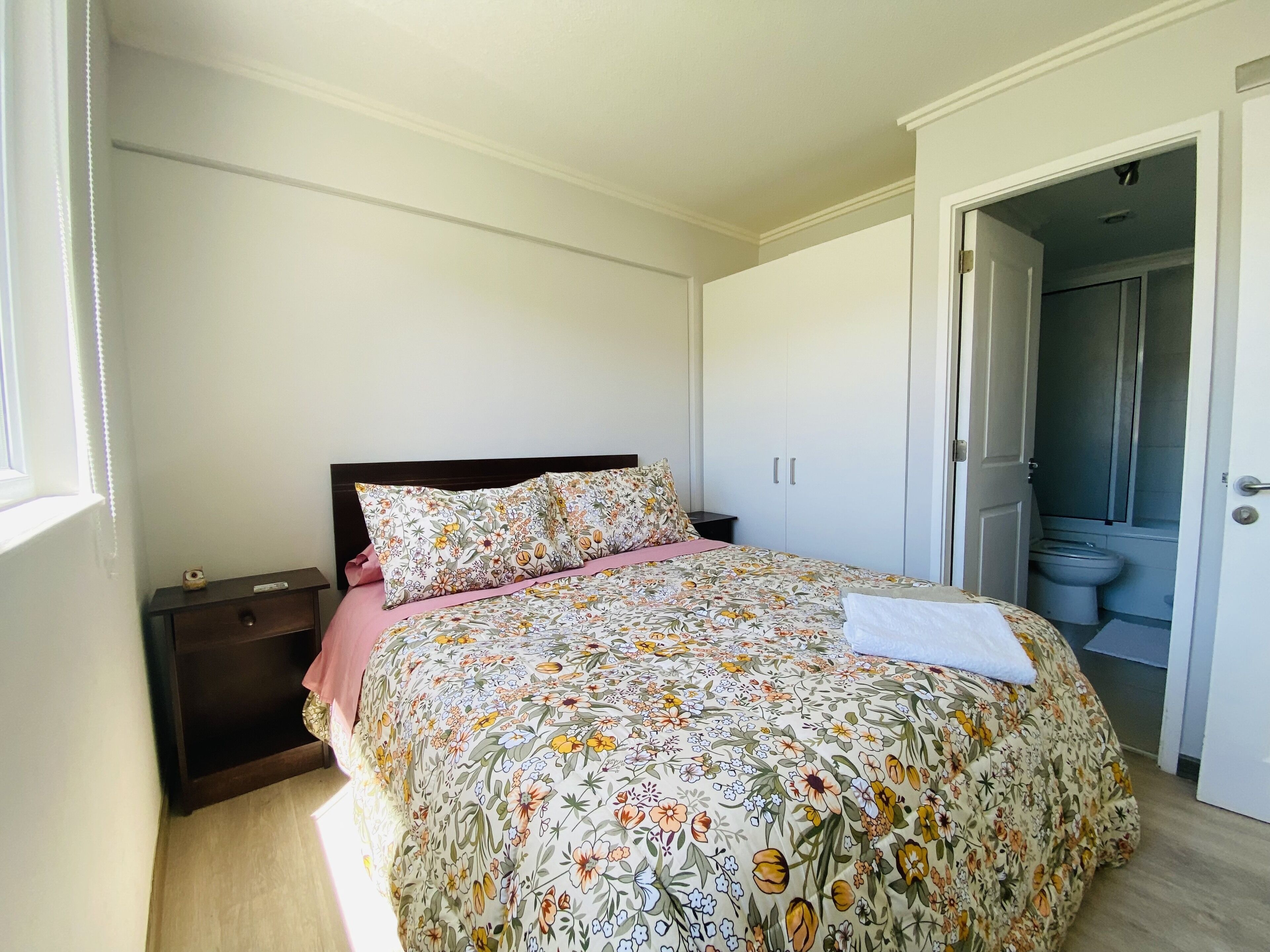 A bedroom with a bed, nightstands, a wardrobe, and a bathroom visible through an open door.