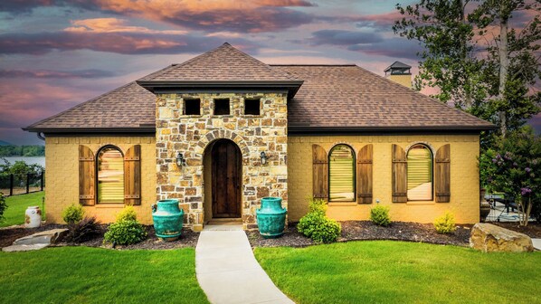 A two-story house with a stone facade, a central entrance, and a small tower-like structure on the roof.