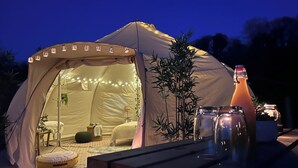 A tent with a bed, pillows, a table with a bottle, and a plant. - Erw Glas Glamping and Camping (Llanrwst)
