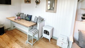 A cozy room with a wooden floor, a white bench with plaid cushions, a small white cabinet, and a mounted mirror. - Erw Glas Glamping and Camping (Llanrwst)