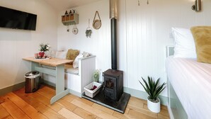 A cozy room with a bed, a small table, a sofa, a wall-mounted TV, a fireplace, and a potted plant. - Erw Glas Glamping and Camping (Llanrwst)