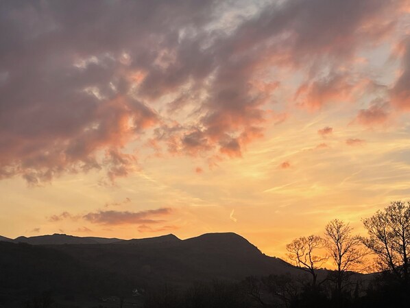 A sunset over a mountainous landscape with silhouettes of trees and a distant building.