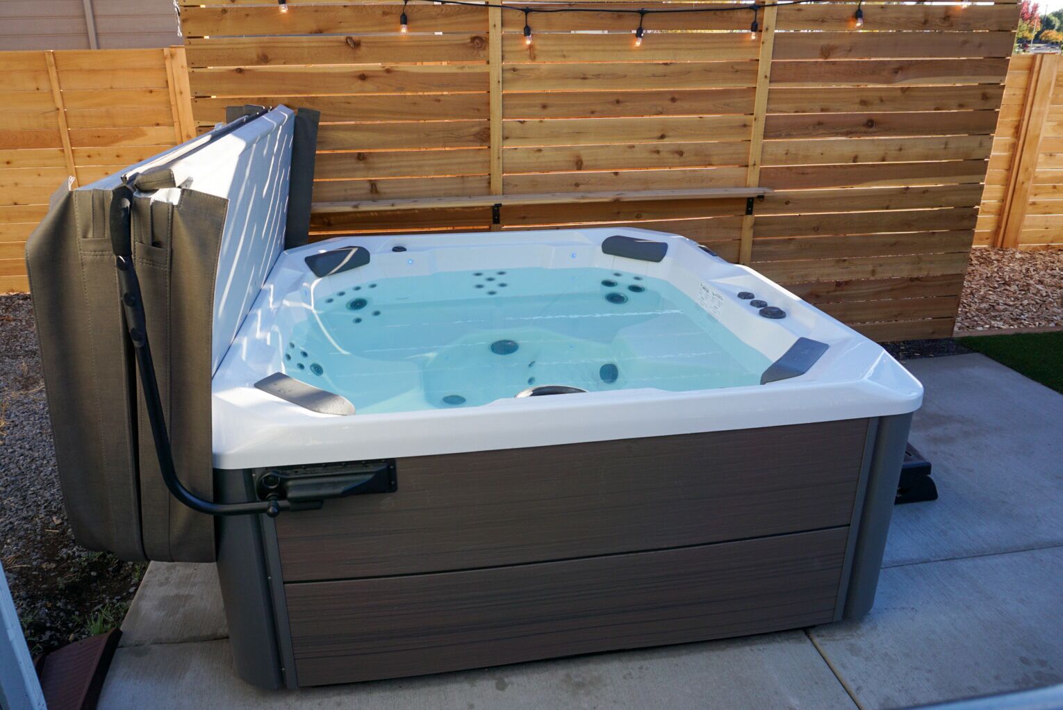 A hot tub with a wooden deck and a wooden fence in the background.