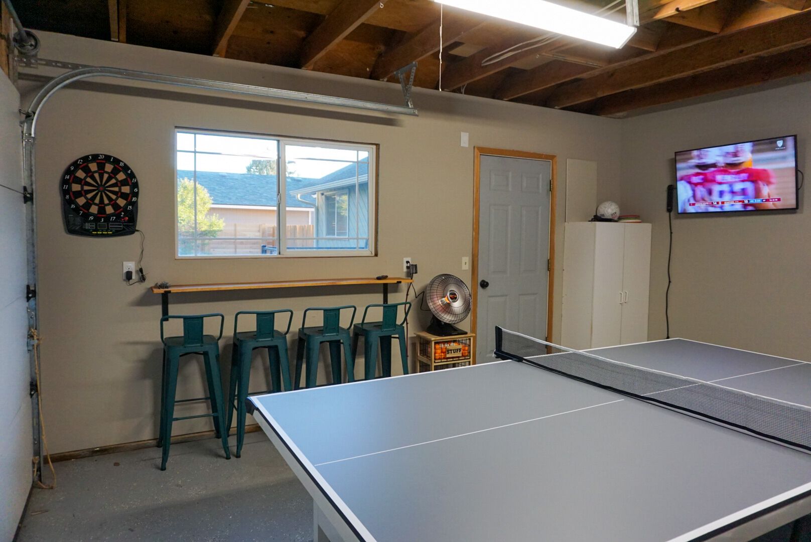 Une pièce équipée d’une table de ping-pong, d’un jeu de fléchettes et d’un téléviseur diffusant un événement sportif.