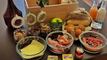 Uma bancada de cozinha com diversos alimentos e ingredientes, incluindo potes de compotas, uma garrafa de chá verde, ovos, pão e carne.