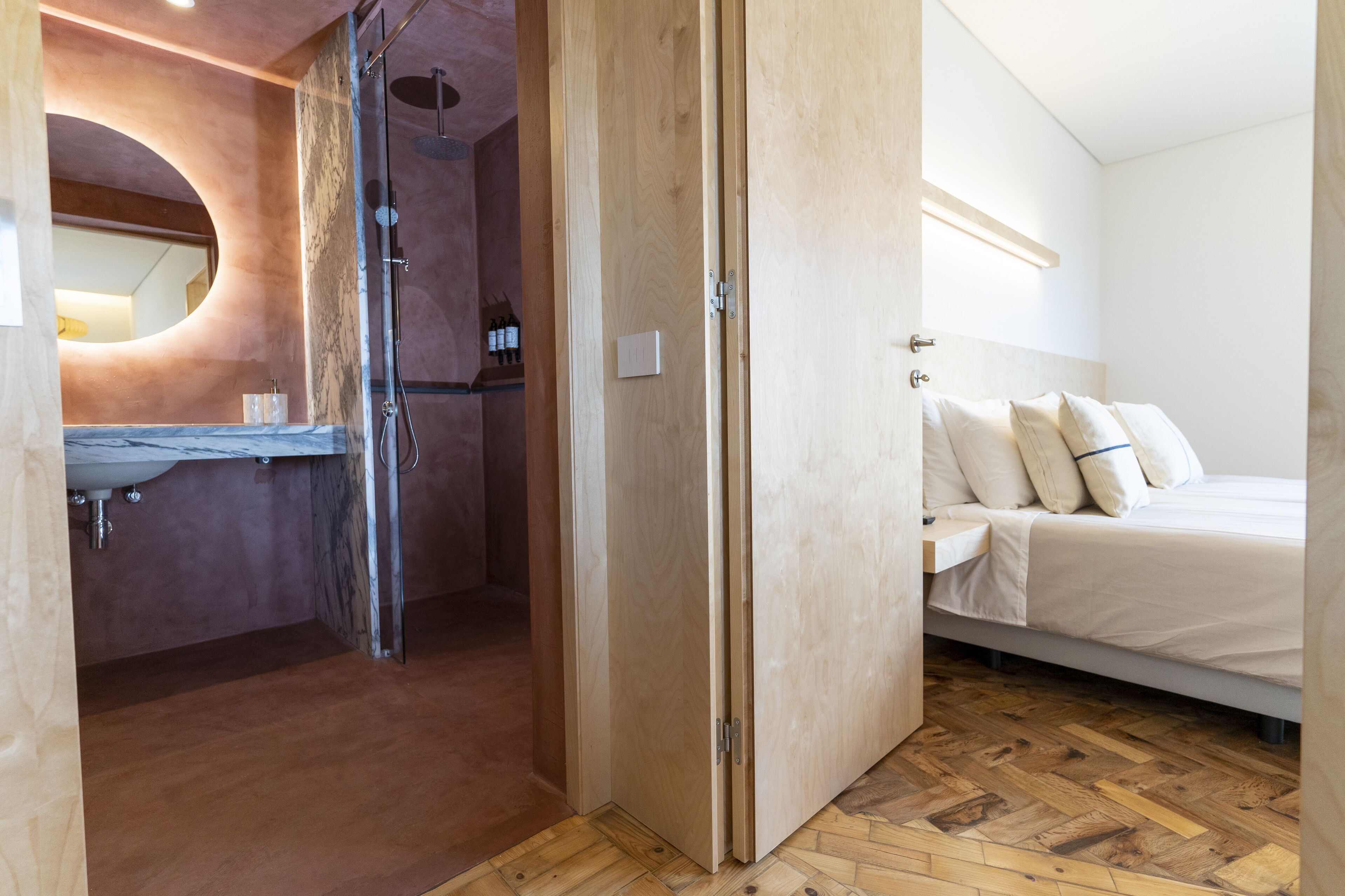 A modern bathroom with a marble sink, a glass shower enclosure, and a wooden floor.