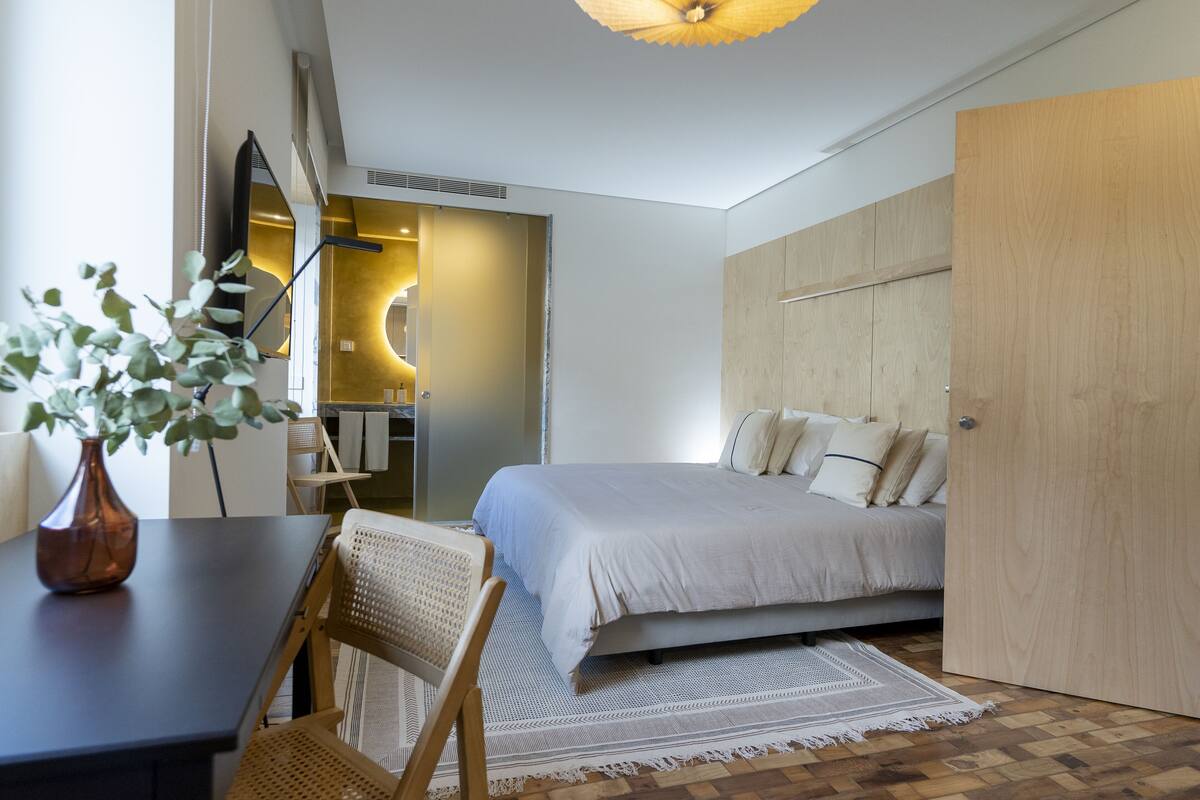 Een moderne slaapkamer met een bed, een bureau, een stoel, een houten garderobe en een spiegel.