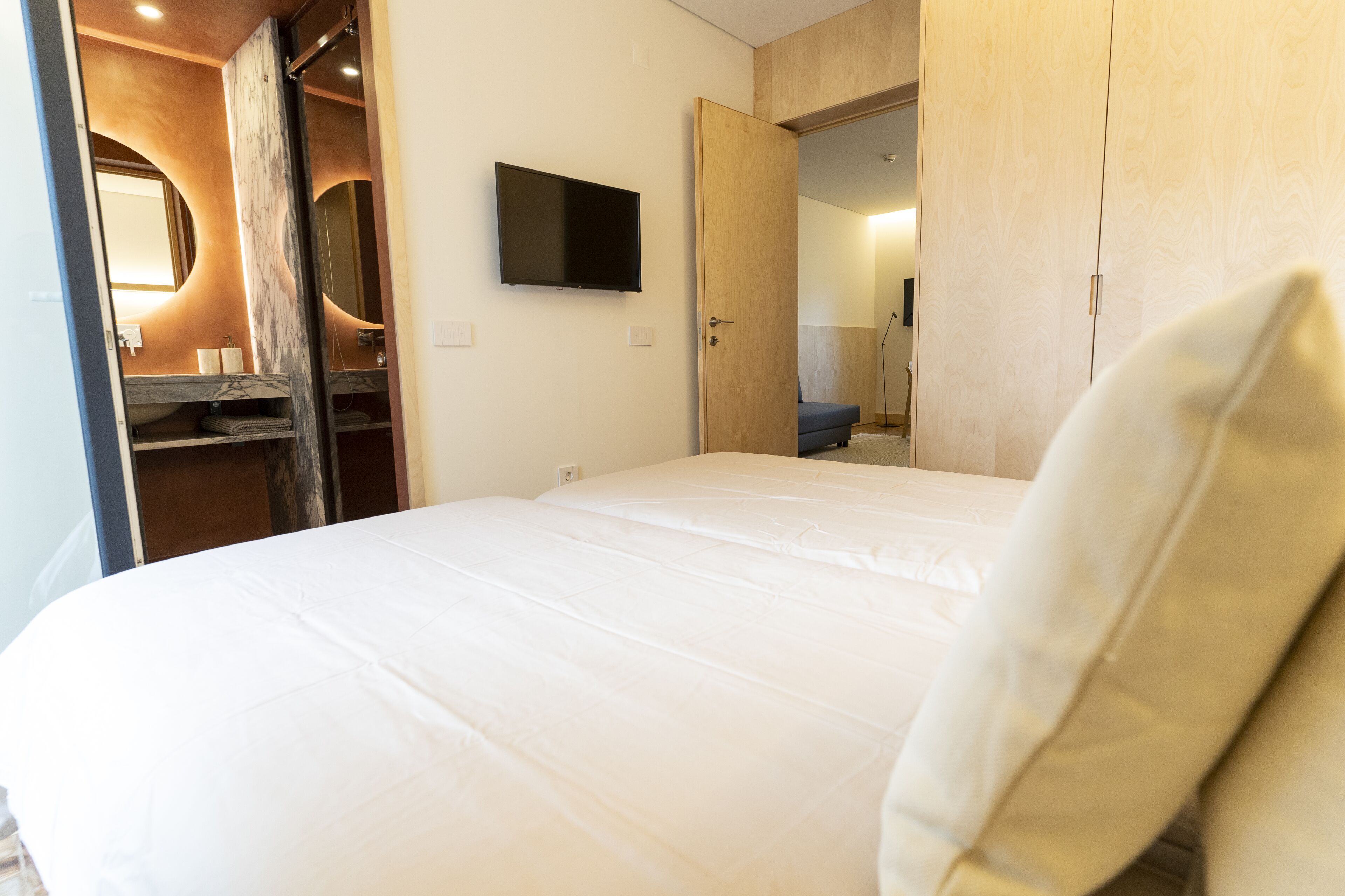 Et hotelværelse med en seng, et fjernsyn ophængt på væggen, et træskab og et spejl.