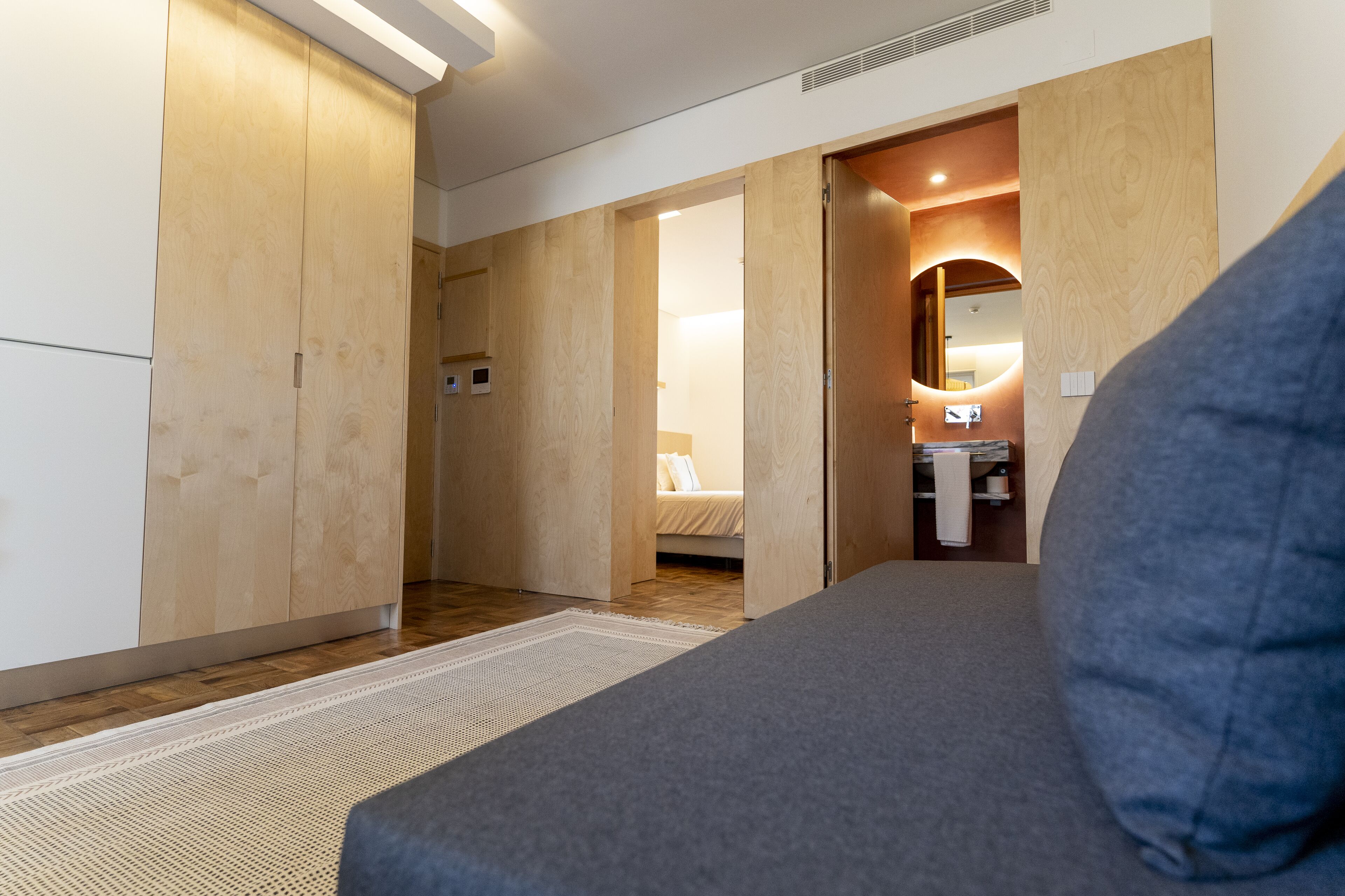 Quarto de hotel moderno com um guarda-roupa grande, uma cama e um banheiro visível através de uma porta aberta.