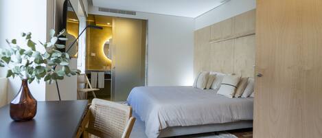 A modern bedroom with a bed, a desk, a chair, a wooden wardrobe, and a small plant.