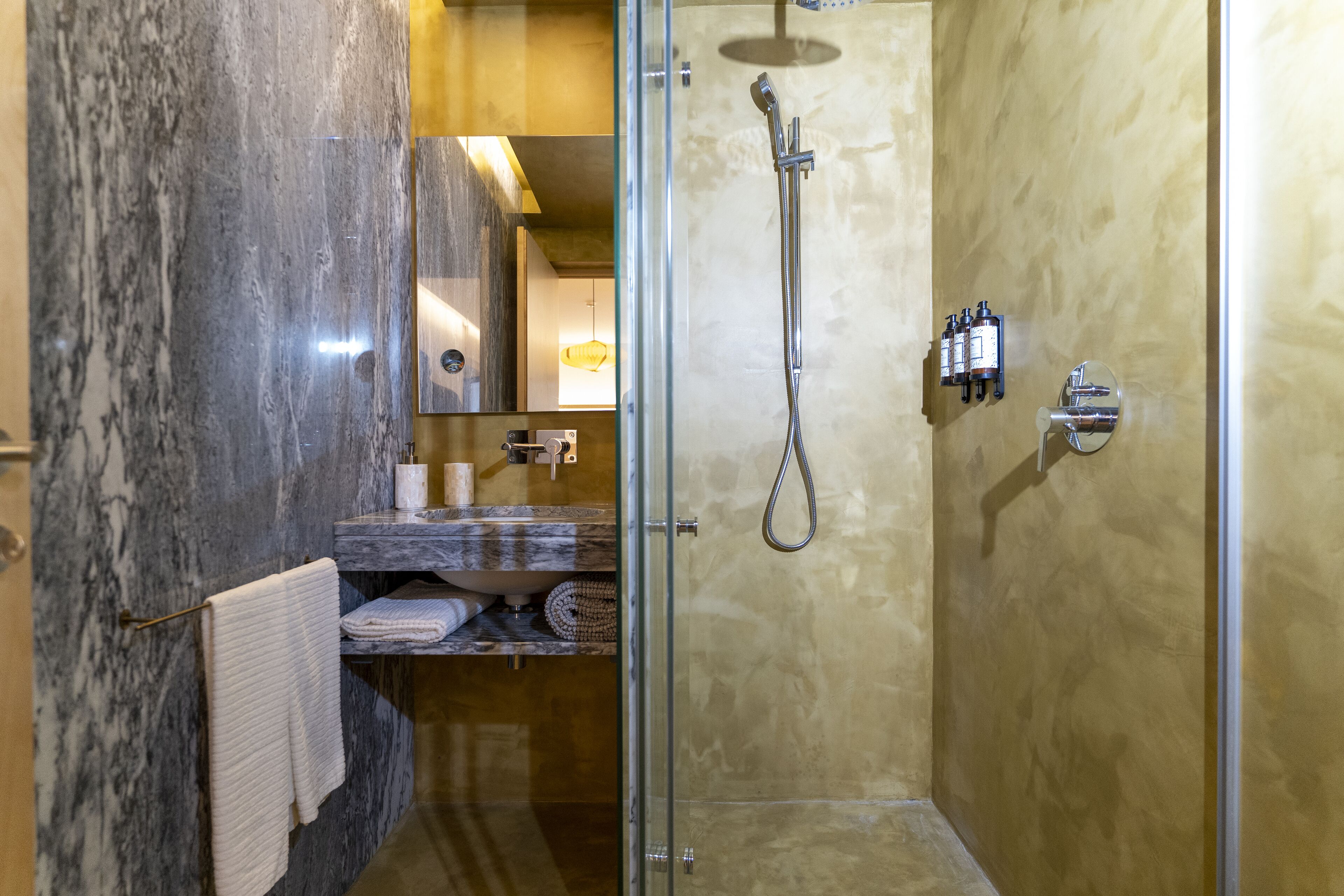 A modern bathroom with a glass-enclosed shower, marble walls, and a wooden vanity with a towel rack.