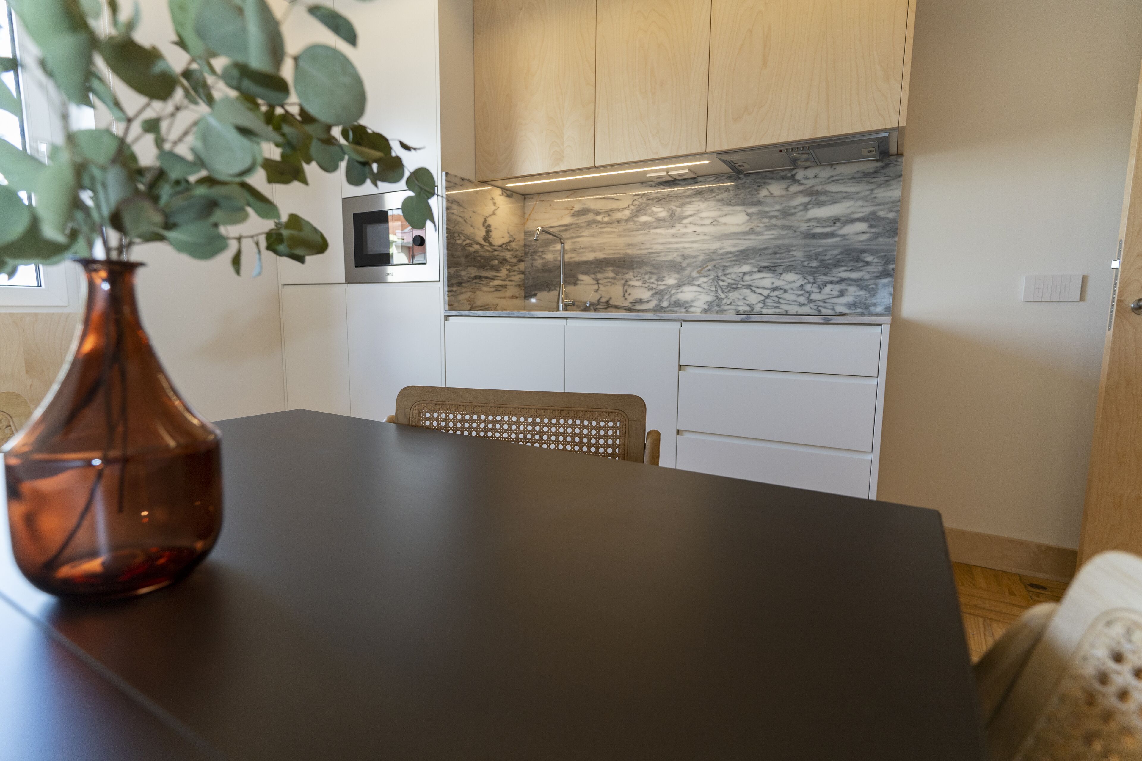 Uma cozinha moderna com painel de mármore, armários de madeira e bancada escura.