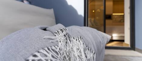 A close-up of a grey sofa with white fringes, positioned in a modern room with a glass door leading to a kitchen area.