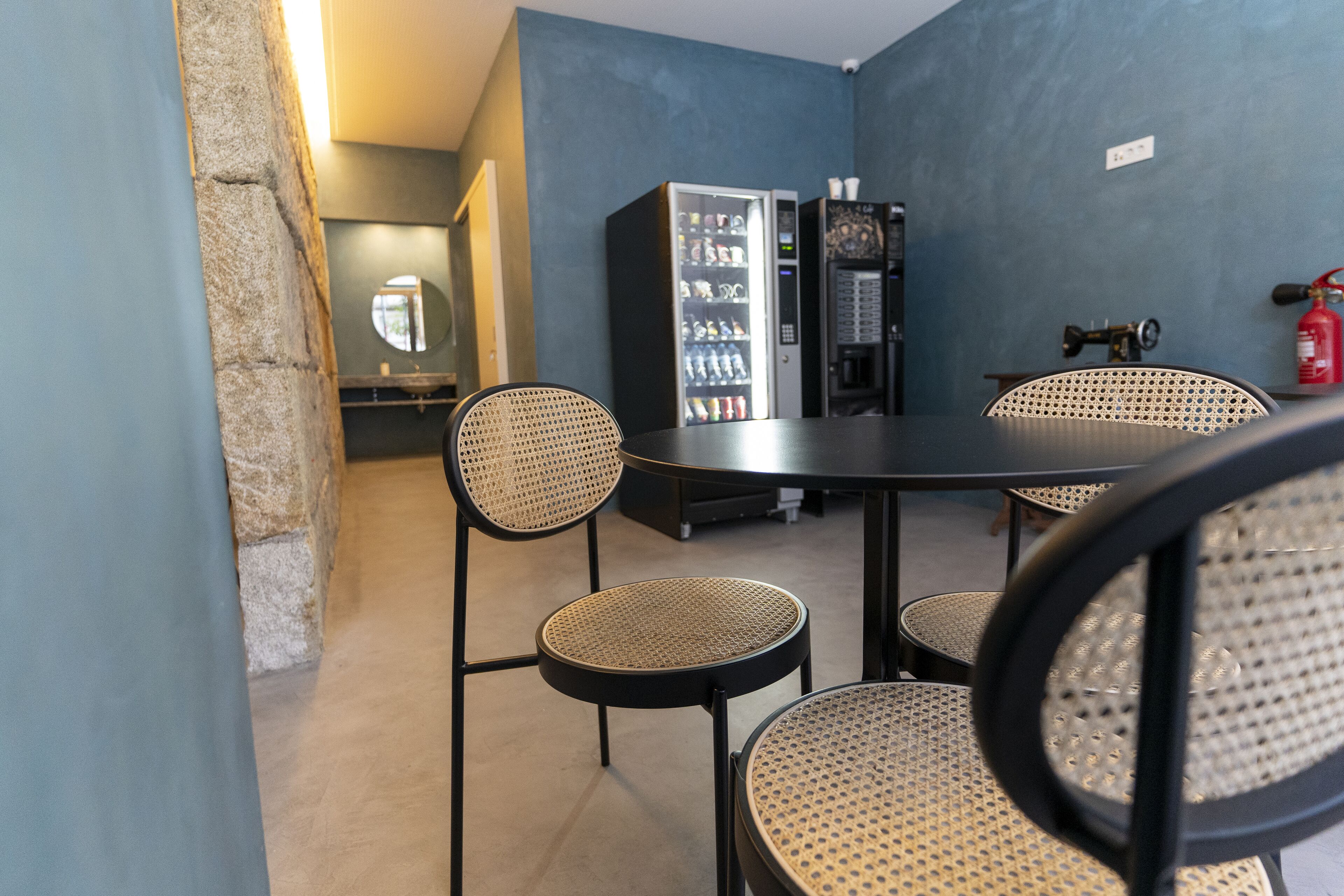 A room with a table and four wicker chairs, a vending machine, and a fire extinguisher.