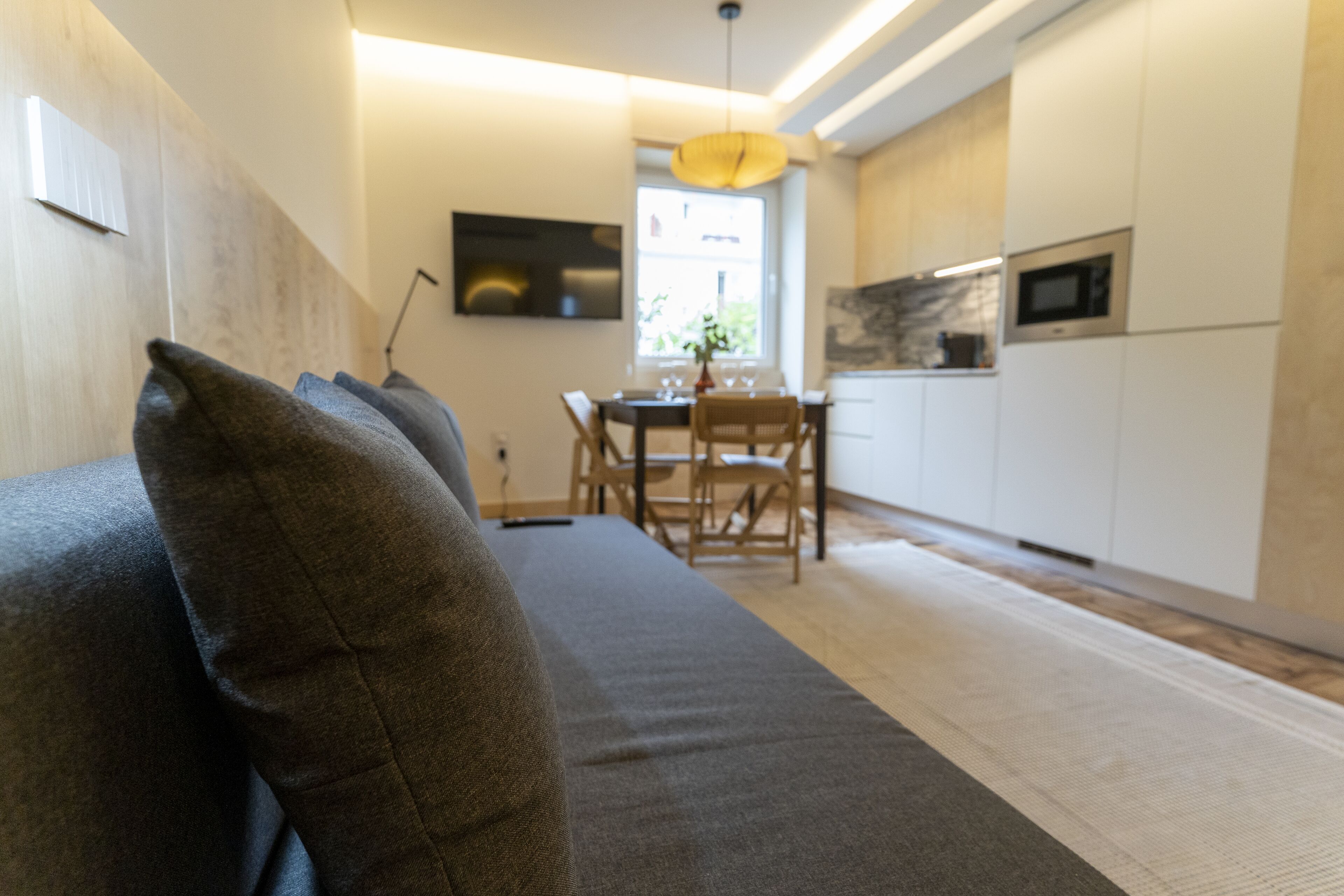 A modern kitchen with white cabinets, a dining area with a table and chairs, and a sofa with cushions.