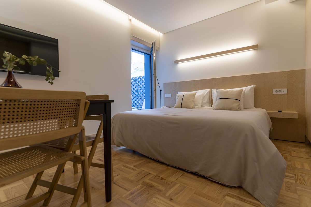Een moderne slaapkamer met een bed, houten vloer en een aan de muur bevestigde televisie.