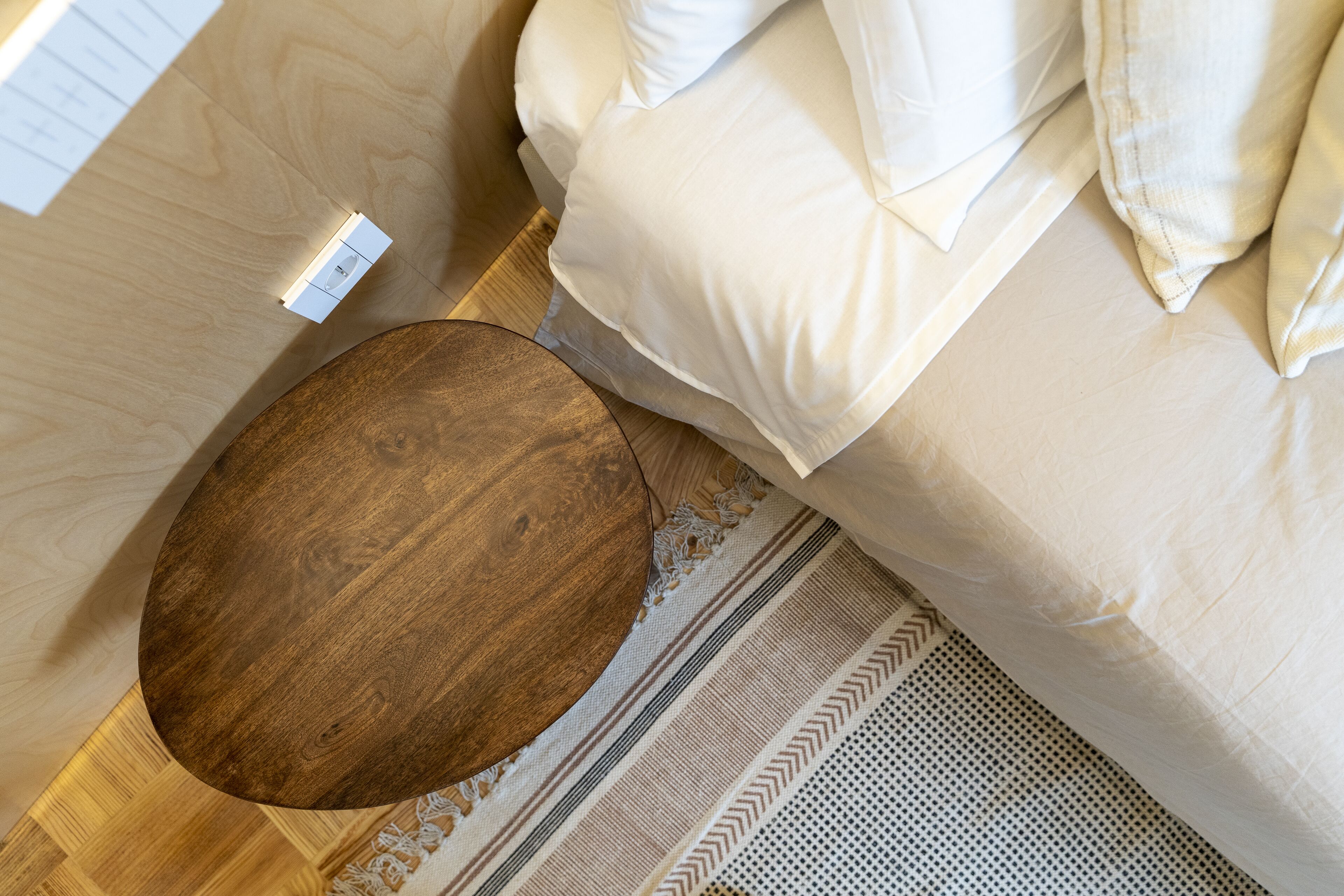 A bedroom with a wooden round table, a bed with white bedding, and a patterned rug.