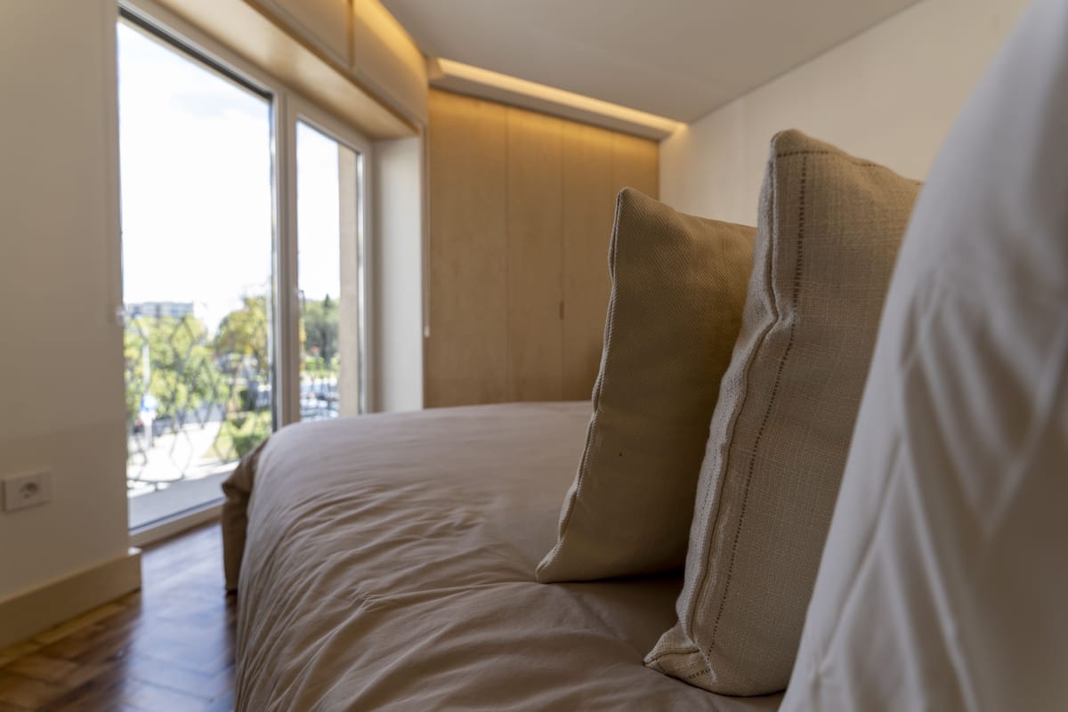 Een slaapkamer met een bed, grote ramen en uitzicht op bomen.