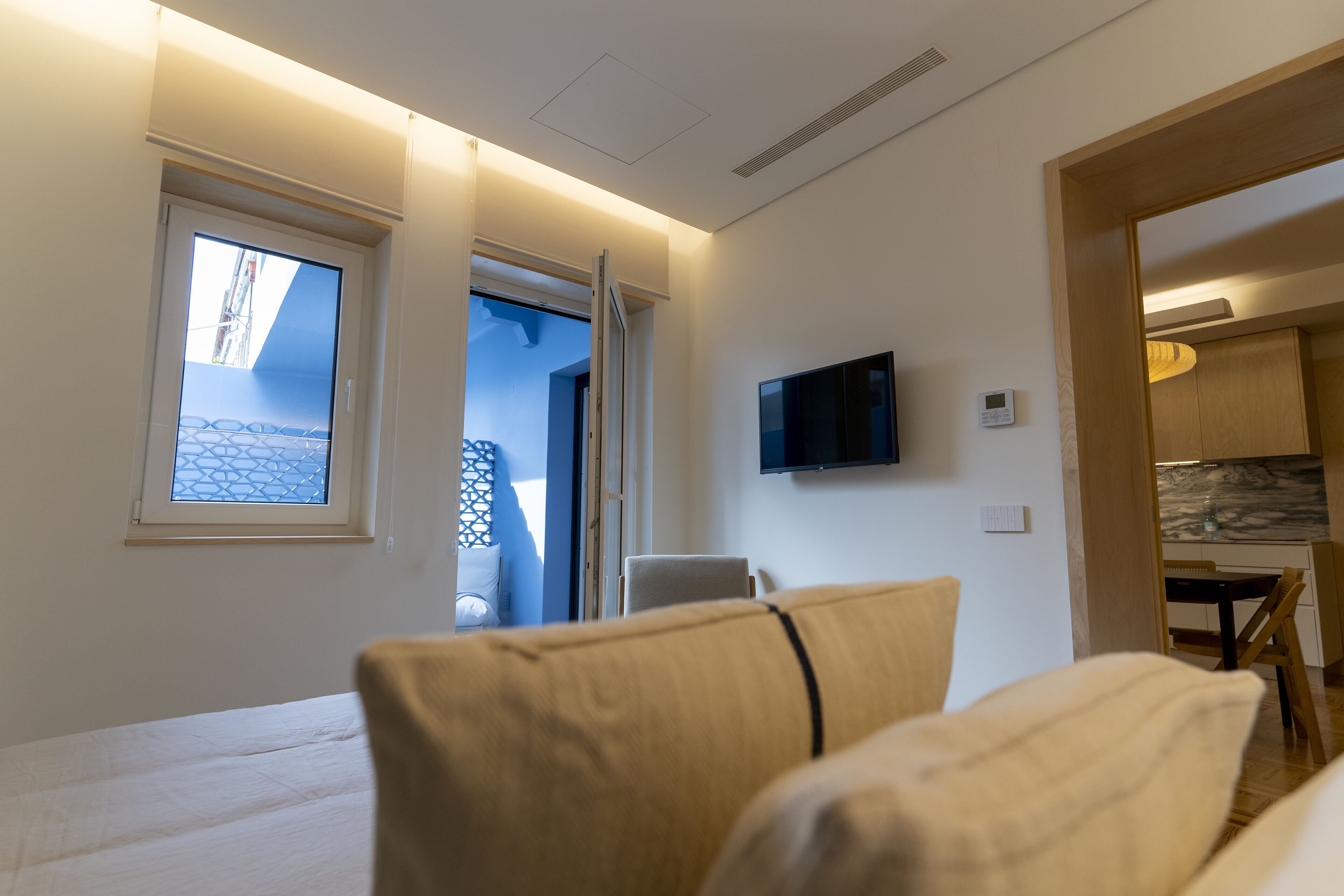 Una habitación de hotel moderna con una cama, un televisor montado en la pared y vistas al balcón exterior a través de una ventana.