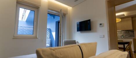 Una habitación de hotel moderna con una cama, un televisor montado en la pared y vistas al balcón exterior a través de una ventana.