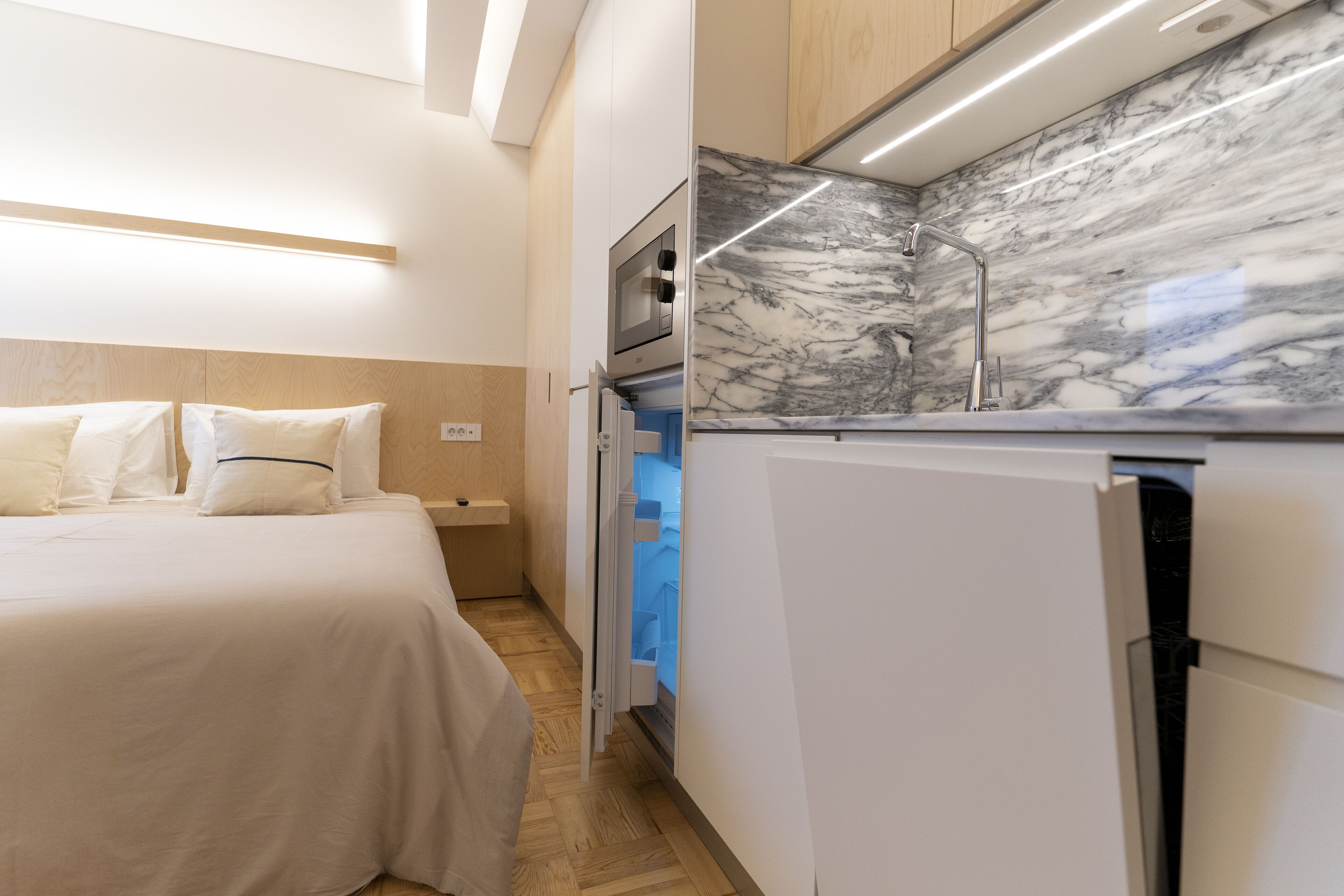 A compact hotel room with a bed, a built-in microwave, and a marble countertop with a sink.