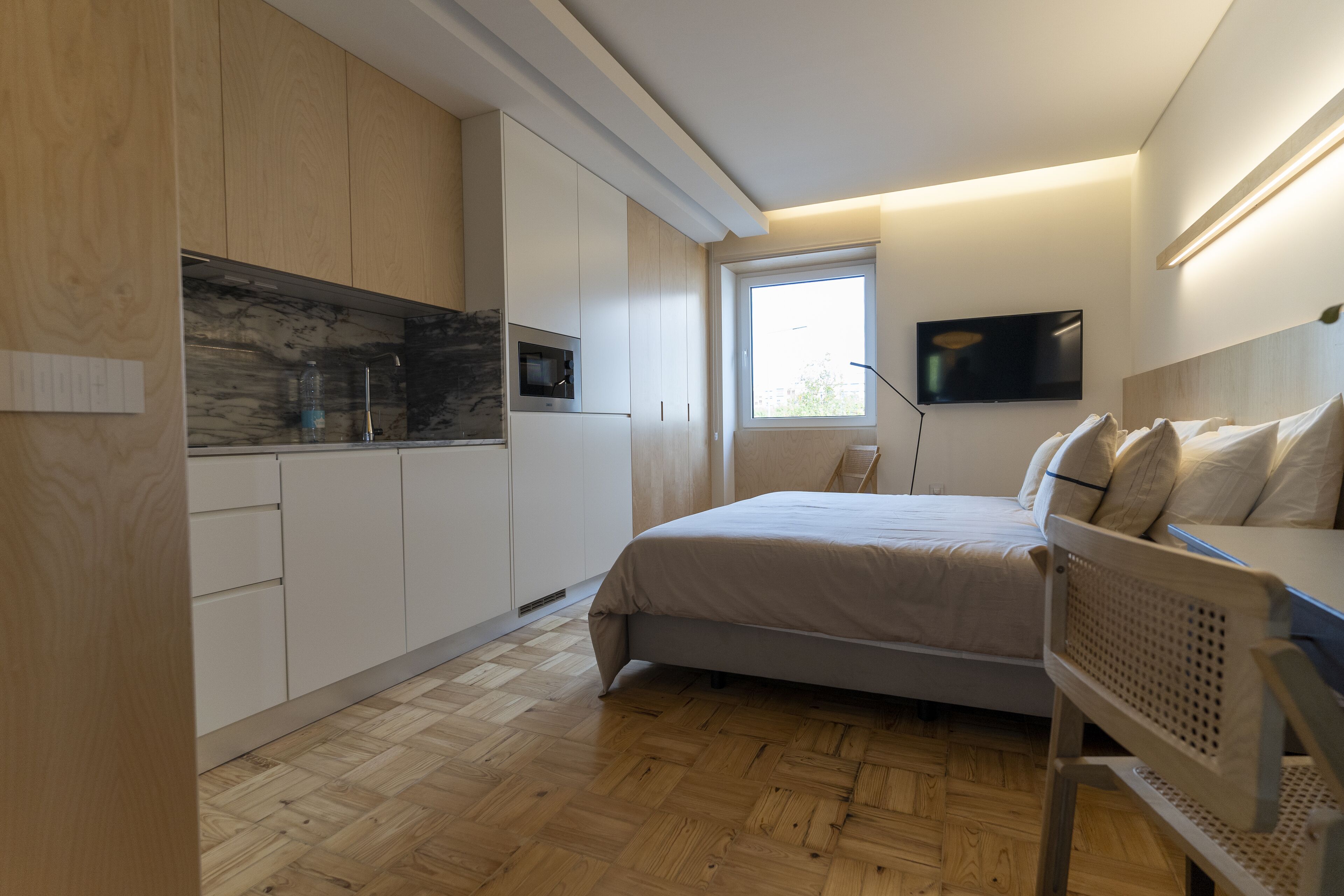 A modern bedroom with a bed, a chair, a TV, and a window.