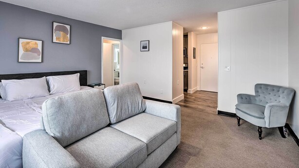 Ein modernes Hotelzimmer mit grauem Sofa, einem Bett mit weißen Leinen und einem grauen Sessel.