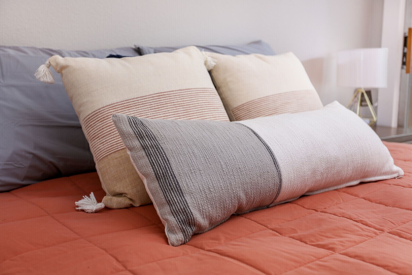 A bed with a red quilt and three pillows in different colors and patterns.