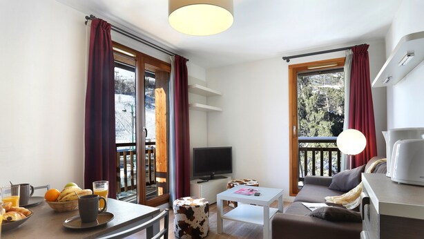 Una sala de estar moderna con sofá, una mesa de centro, televisor y un balcón con cortinas.