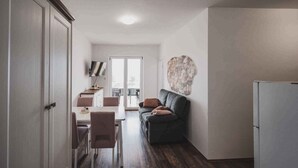A modern kitchen with a refrigerator, a dining area with a table and chairs, and a living area with a sofa and a decorative wall piece. - Holiday apartment with sea view, air conditioning and close to the beach (Klimno)