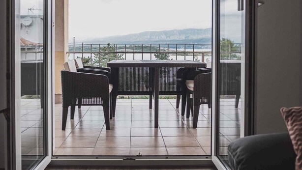 A room with a sliding glass door leading to an outdoor balcony with a table and chairs. - Holiday apartment with sea view, air conditioning and close to the beach (Klimno)