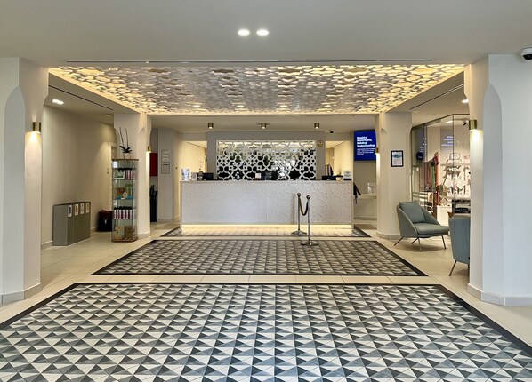 Un área de recepción moderna con suelo estampado, un mostrador y una zona de estar con sillas.
